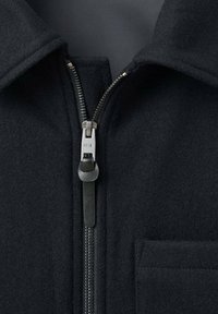 Chaqueta de lana negra con cremallera frontal, tirador de cuero y un bolsillo parche en el lado izquierdo. Tejido texturizado y cuello entallado.