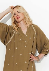 Robe vert olive avec des manches volumineuses, présentant une broderie florale blanche et un décolleté en V avec un détail de bouton. Texture de tissu douce.