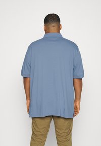 Blå kortärmad polotröja gjord av bomull, med en klassisk krage, avslappnad passform och diskreta sidofickor vid nederkant.