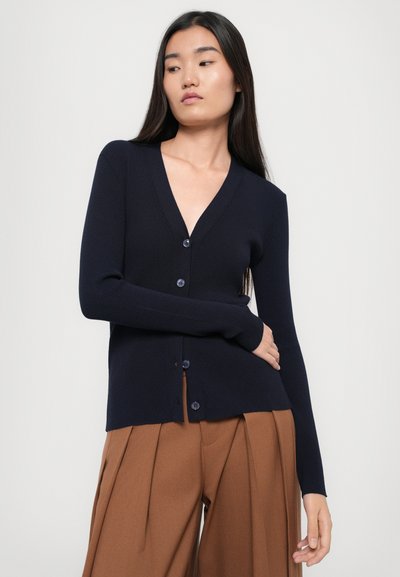 Navy ribbed cardigan with a V-neck, long sleeves, and six blue buttons down the front. Paired with brown wide-leg trousers.