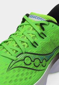 Φωτεινό πράσινο παπούτσι τρεξίματος Saucony με μαύρο λογότυπο, επάνω μέρος από δίχτυ και ασορτί πράσινα κορδόνια δεμένα χαλαρά.