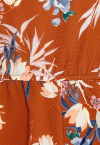Tecido com padrão floral em laranja enferrujado, apresentando flores brancas e azuis. Textura suave com detalhe de costura franzida para o design.