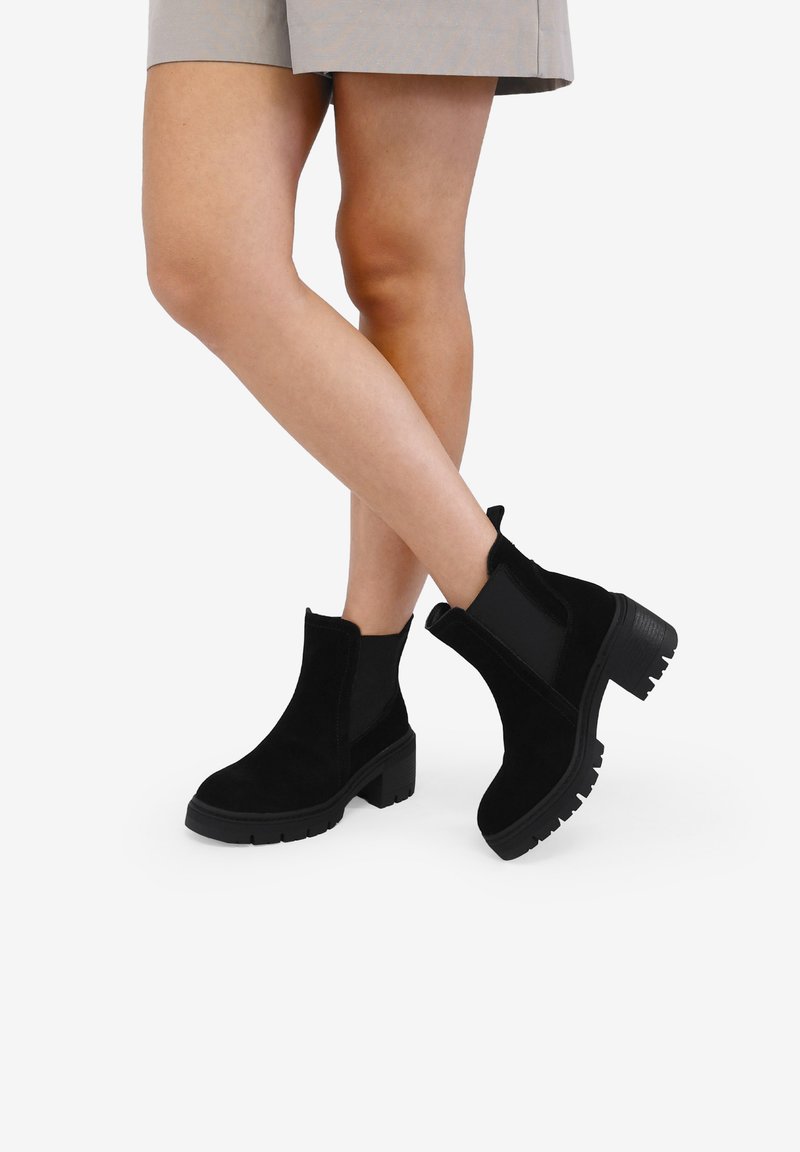 Botas de tobillo de ante negro con una suela gruesa y un tacón ligeramente grueso. Presentan paneles laterales elásticos y un diseño de punta redonda.