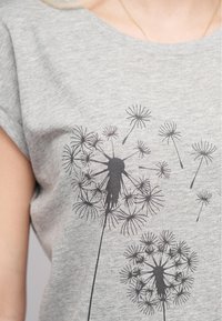 T-shirt en coton gris à manches courtes, arborant un motif graphique de pissenlit noir avec des têtes de graines et des tiges détaillées.