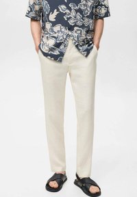 Lichtbeige linnen broek, gesneden pasvorm, gecombineerd met een marineblauwe bloempatronen overhemd met korte mouwen. G gedragen met zwarte kruisband sandalen.