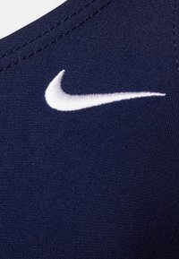 Tissu de sport bleu marine avec une texture lisse, arborant un logo Swoosh Nike brodé en blanc près du col.
