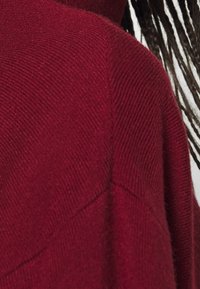 Bordeaux stickad tröja med en avslappnad silhuett, subtil diagonal textur och en bred halsringning. Mjuk, medelviktig tyg.