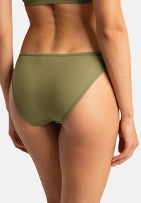 Bas de bikini côtelé en vert olive, avec une taille mi-haute et une texture lisse. Le design met en valeur les courbes avec une couverture minimale.