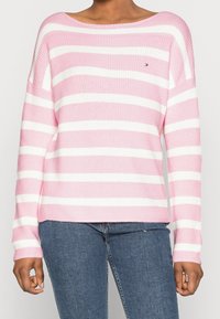 Pull-over rayé en rose clair et blanc. Il présente un large col, des manches longues et une texture côtelée. Logo sur la poitrine gauche.
