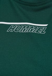 Camiseta de tela verde acanalada con un logotipo blanco de "HUMMEL" en el pecho, con cuello redondo y superficie texturizada.