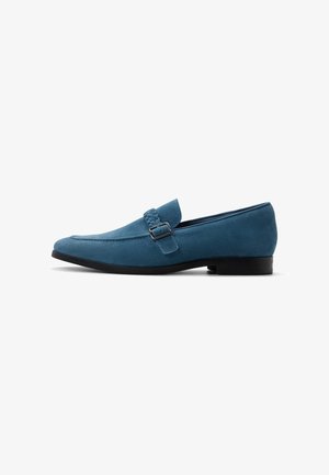 Blauwe suède loafer met gevlochten band en zilveren gesp, lage zwarte hak en puntige neus, zijaanzicht op witte achtergrond.