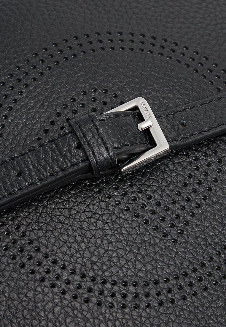 Schwarzer strukturierten Leder Gürtel mit silberner rechteckiger Schnalle, die auf einer perforierten Lederoberfläche liegt und ein geometrisches Muster bildet.
