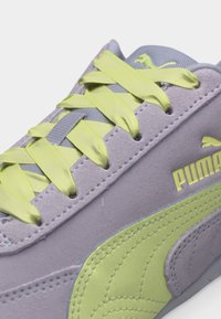 Közelkép egy szürke Puma tornacipőről sárgászöld szatén fűzőkkel, Puma logóval és hozzáillő sárgászöld oldalsáv díszítéssel.