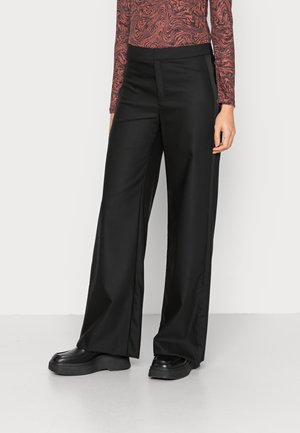 Person wearing high-waisted black wide-leg pants, black platform shoes, and a long-sleeve top with a red and black abstract pattern.
