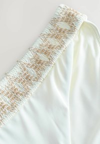 Vita badbyxa med ett strukturerat, beige vävt elastiskt midjeband. Slätt tyg med en lätt glänsande yta. Inga mönster eller ytterligare detaljer.