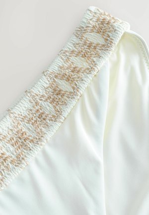 Vita badbyxa med ett strukturerat, beige vävt elastiskt midjeband. Slätt tyg med en lätt glänsande yta. Inga mönster eller ytterligare detaljer.