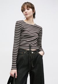 Pruuni ja kreemika triibulise pika varrukaga top, millel on kärbitud lõige ja vöökoha pael, sobitatud kõrge vöökohaga tumedate teksadega.