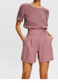 Blouse en lin rose clair à manches courtes associée à un short taille haute plissé avec poches latérales et détails à boutons.