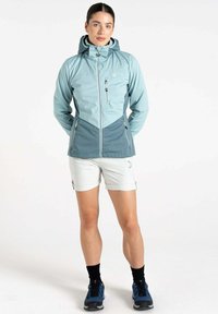 Hellblaues und dunkelblaues Zip-Jacke mit Kapuze, versehen mit schr�ägen Nähten und Seitentaschen. Kombiniert mit hellen Shorts und schwarzen Socken.