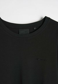 Czarna bluza z okrągłym dekoltem z prążkowanym wykończeniem, z małym wytłoczonym logo w dopasowanym kolorze, wykonana z miękkiego materiału o gładkiej fakturze.