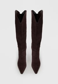 Bottes en suède marron foncé, arrivant jusqu'aux genoux, avec un bout pointu et un bord supérieur en V fendu. Texture lisse avec des détails matériels minimaux.
