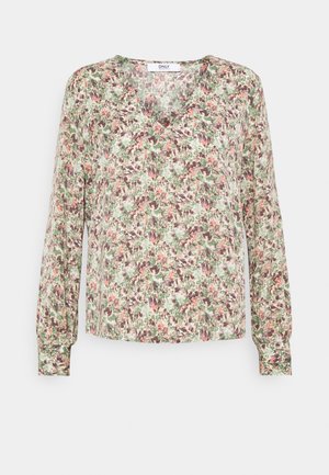 Blouse à manches longues et col en V avec un motif floral vert, marron et rose et des poignets boutonnés sur fond clair.