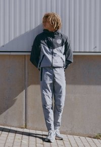 Gray athletic tracksuit with black accents, featuring a zip jacket and elastic waistband pants. Logo on the jacket, lightweight fabric.