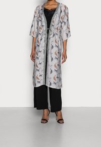 Lättvikts, knälång kimono i genomskinlig grått tyg med färgglada kattmönster. Knuten i midjan med ett mönstrat kantband och vida ärmar.
