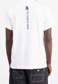 Vit bomull t-shirt med ett vertikalt svart och blått grafiskt tryck av "THE NORTH FACE" på baksidan, med korta ärmar och klassisk passform.