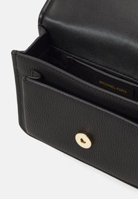 Zwarte leren handtas met een gestructureerd oppervlak, voorzien van een goudkleurige drukknoopsluiting en interne kaartsleuven. Compact ontwerp voor gemakkelijke draagbaarheid.