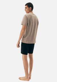 Szara bawełniana koszulka z krótkim rękawem, w połączeniu z czarnymi szortami. Model stoi boso, lekko odwrócony od aparatu.