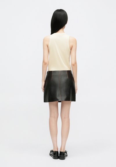 Melnas ādas minibikses ar redzamām šuvēm, apvienotas ar pieguļošu bēša krāsas topu. Gluda tekstūra un taisna siluets.