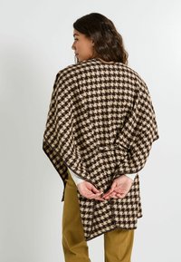 Poncho à carreaux marron et beige avec une ouverture devant et des coutures sur les côtés, doté d'un lien à la taille. Le tissu semble doux avec une finition texturée.