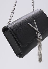Black textured leather handbag with a silver chain strap, featuring a metallic V accent and a tassel detail. Compact design for easy carrying.