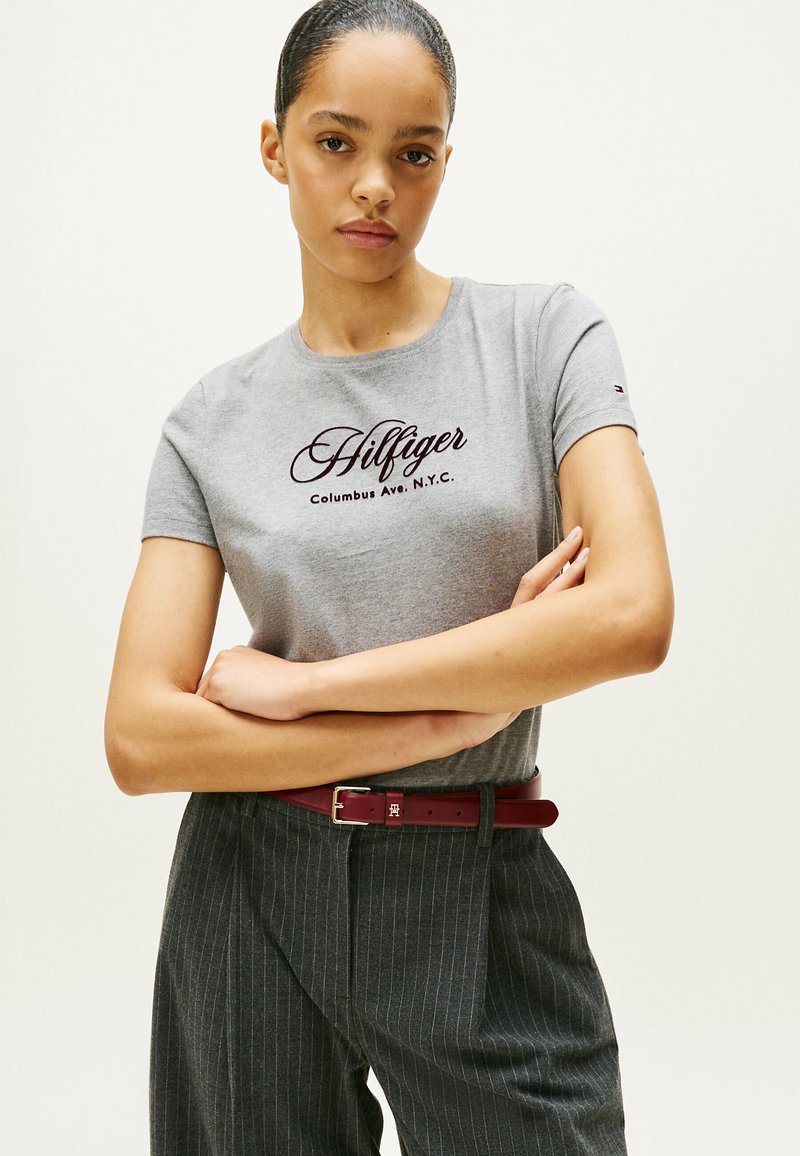 Grå bomulds t-shirt med runde halsudskæring, der har mørk maroon "Hilfiger" tekst. Parret med stribede bukser og et bordeaux-bælte.