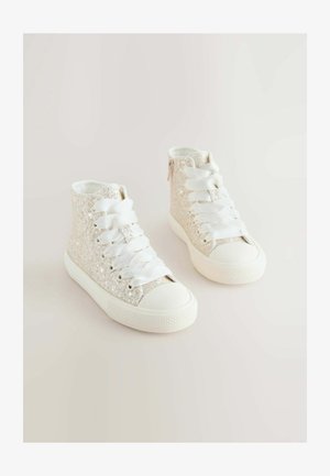 Csillogó ezüst felsőrésszel rendelkező magas szárú sportcipők, fehér fűzőkkel és gumitalppal. Kerek orrú kialakítással és oldalsó cipzárral a könnyű felhúzás érdekében.