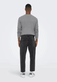 Harmaa tekstuuri neule yhdistettynä mustiin korkeavyötäröisiin farkkuihin. Farkuissa on takataskut. Valkoiset tennarit, joissa on vihreitä yksityiskohtia, täydentävät asun.