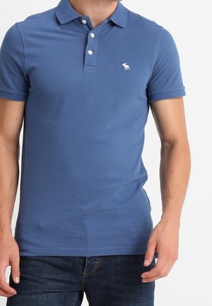 Niebieska koszulka polo z bawełny, z trzema guzikami, krótkimi rękawami i białym logo wyszywanym na piersi.