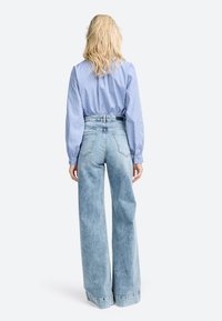 Jean large en denim bleu clair avec une taille haute et des poignets retroussés ; associé à un chemisier rayé à manches longues en bleu et blanc.