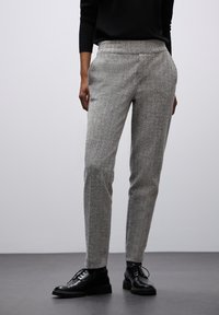 Grijze tweed broek met een getailleerde pasvorm, voorzien van een vlakke voorkant, zijzakken en een soepele tailleband. Gecombineerd met zwarte veterschoenen.