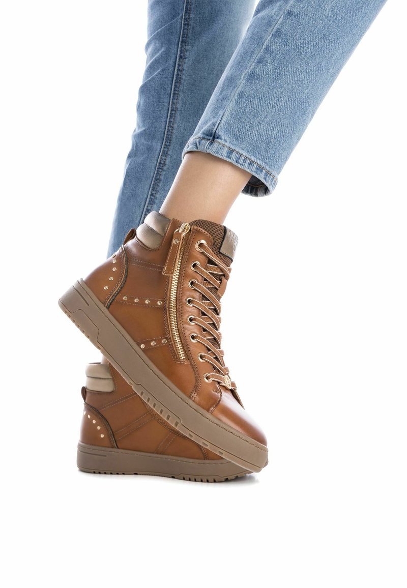 Zapatillas altas marrones de cuero, con cierre de cremallera, cordones, detalles con tachuelas y una suela de goma gruesa.
