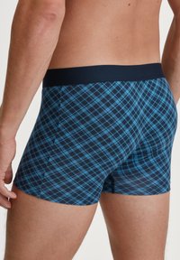 Boxer brief da uomo blu a quadri con una cintura navy scura. Il tessuto presenta un motivo a scacchi con diverse tonalità di blu. Texture morbida.
