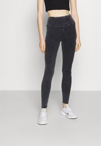 Svarta, högmidjade leggings med en slät textur och ett urblekt mörkgrått mönster, tillsammans med vita träningsskor.