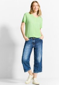 Lys grøn kortærmet skjorte, afslappet pasform; parret med cropped, falmede blå jeans; hvide sneakers fuldender outfittet.