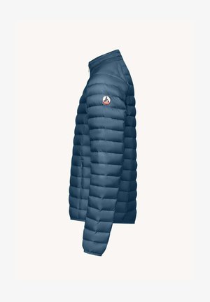 Chaqueta acolchada en azul oscuro, con cuello alto, cierre de cremallera y parche con logo en la manga. Textura suave con patrón acolchado.