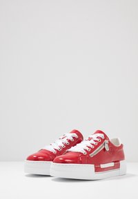 Baskets en cuir verni rouge avec des lacets blancs, dotées d'une fermeture éclair sur le côté, d'une semelle blanche épaisse et de détails en fausse couture.