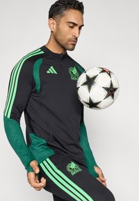 Fekete sportos felső zöld díszítéssel, cipzárral, hosszú ujjú, logóval. Fekete nadrág zöld csíkokkal és logóval. Fehér focilabda fekete csillagokkal.