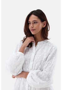 Weiße bestickte Bluse mit durchgehender Knopfleiste, die mit floralen Mustern und puffigen Ärmeln versehen ist. Aus leichtem, durchscheinendem Stoff gefertigt.