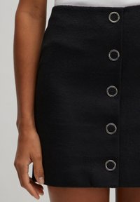 Zwarte wol mini-jurk met een gladde textuur, met vijf zilveren oogjes knopen aan de voorkant voor sluiting.