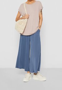 Top rosa chiaro a maniche corte con scollatura rotonda, abbinato a pantaloni larghi blu a gamba larga e una borsa intrecciata beige, completato da sneakers color crema.